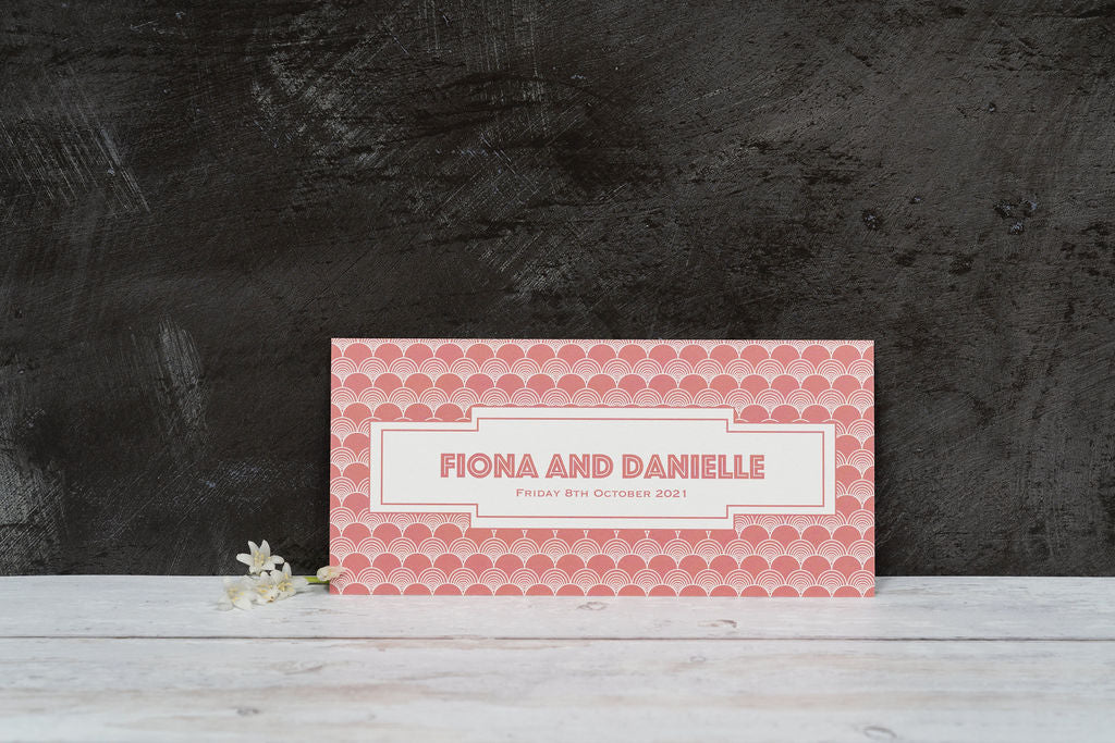 Image copyright EKR Studio. Bookmark-style wedding invitation, with a Gatsby-style pattern and blush background. View of the back, with the couple's names and the date of their wedding.