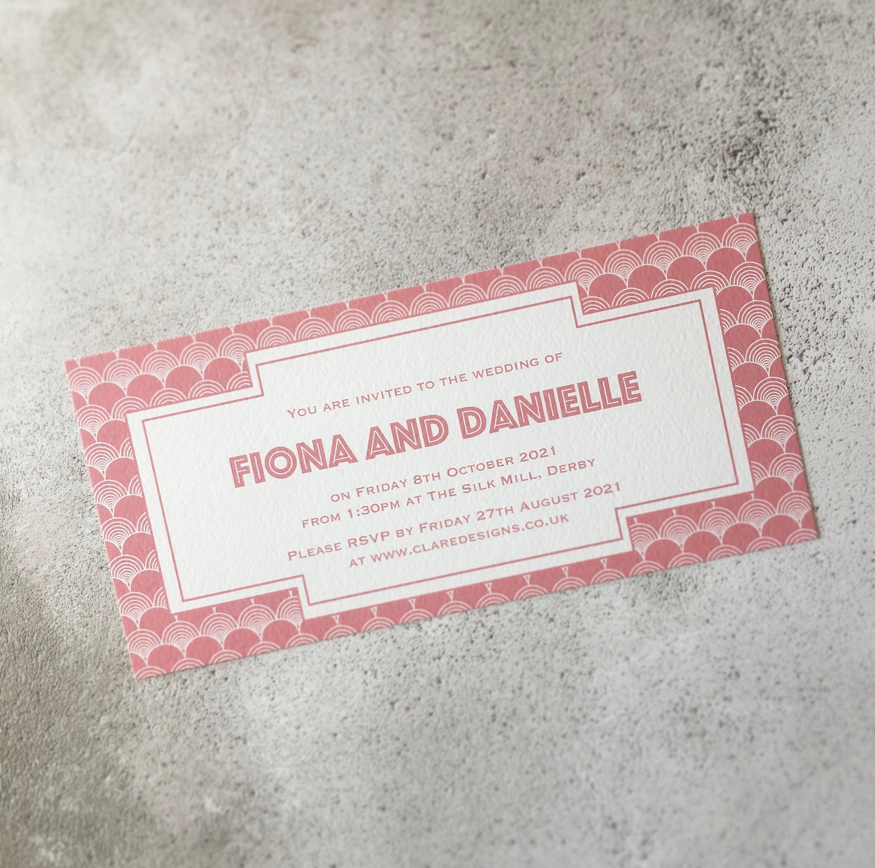 Bookmark-style wedding invitation. Gatsby-style patterned background, with all the wedding details written in a blush text inside a white geometric box.