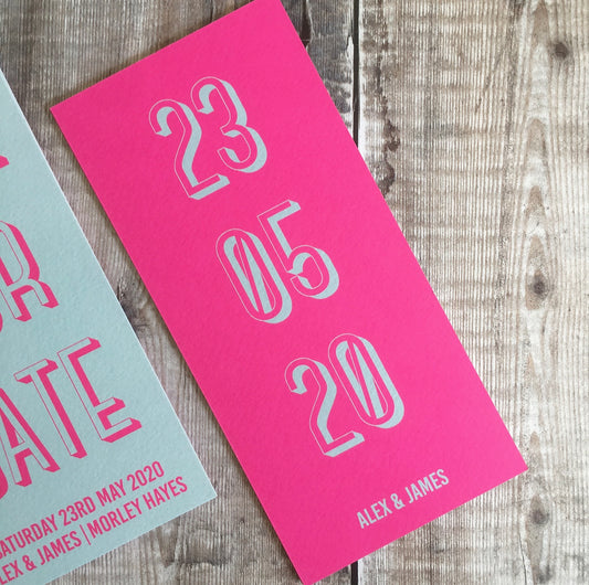 Bookmark-style wedding invitation/save the date. Back view. This has a pink fluorescent background, with the date of the wedding in a teal colour. The overall style is typographic and bold.